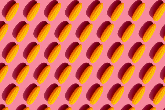 Pattern of yellow plastic corn cobs against pink background