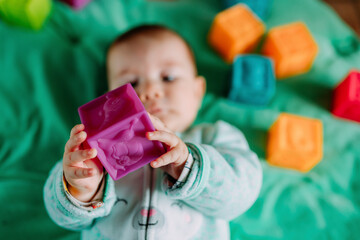 Baby's hands holding purple rubber cube toy, close-up