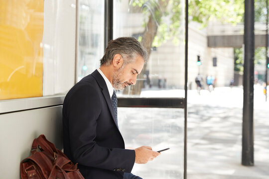 Businessman using phone while sitting at bus stop