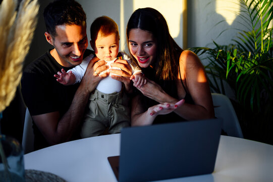 Smiling couple holding son while talking on video call through laptop sitting at home