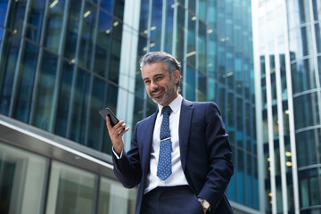 Smiling businessman using mobile phone outside office building in city