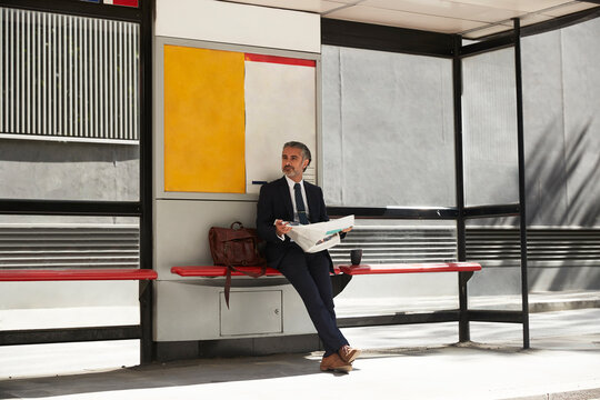 Businessman with newspaper waiting at bus stop