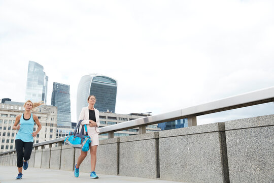 Woman running by businesswoman carrying bag on footbridge in city against clear sky