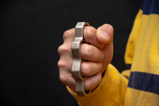 Male hand squeezes metal brass knuckles on a black background.  Concept: grievous injuries and injuries, street fights, fights without rules, urban crime.