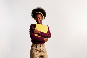 African American girl in brown sweater poses with her yellow folder while listening to music. - 462724266