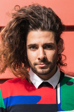 Young man with long hair standing against red wall