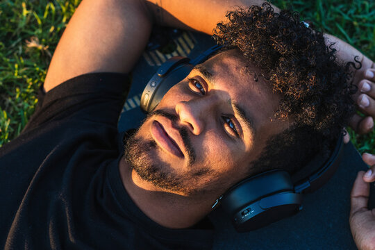 Close-up of thoughtful man listening music over headphones while lying on skateboard in park