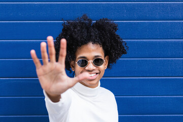 Smiling boy showing stop gesture while standing against blue wall
