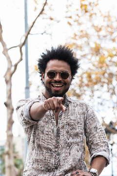 Stylish man wearing sunglasses laughing and pointing while sitting against sky