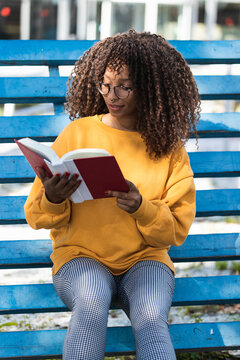 Fashionable young woman reading book while sitting on blue bleachers