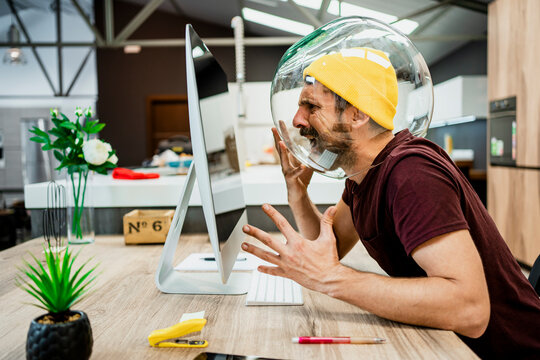 Frustrated businessman with fishbowl in head screaming while using computer in modern office