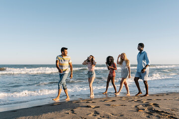 Young friends walking on beach during sunny day