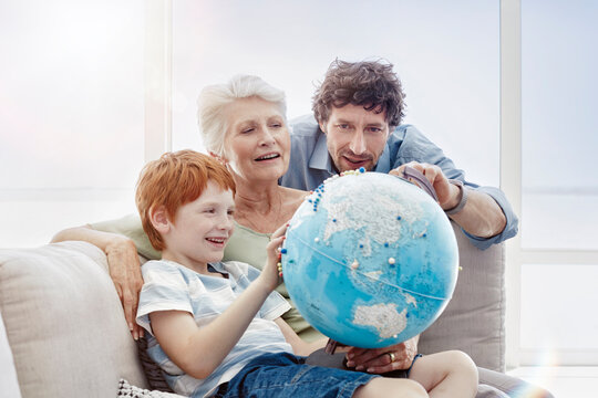 Grandmother, father and grandson sitting on couch in a villa looking at globe