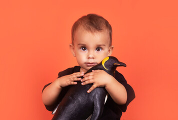 Cute baby girl hugging penguin toy while sitting against orange background