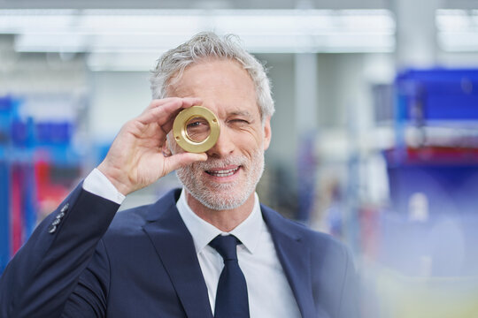 Confident male manager looking through brass object in factory