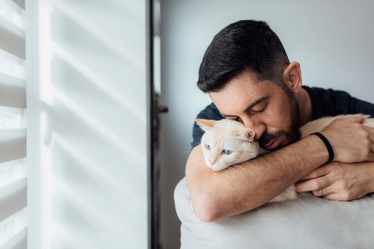 Mid adult man embracing cat in arms while sitting at home