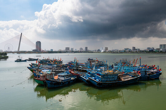 Vietnam, Da Nang, Storm clouds over old fishing boats moored in city harbor