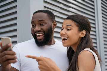 Young happy friends using mobile phone shopping online, focus on African man face