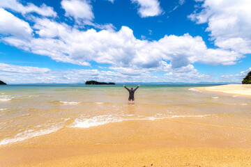 Rear view of mature man standing with arms raised in sea against cloudy sky at Abel Tasman Coastal Track, South Island, New Zealand