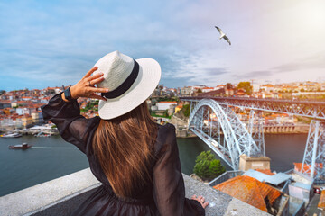 Young woman tourist enjoying beautiful view of Porto city and famous Dom Luis I Bridge at sunset. Summer holiday vacation in North Portugal. - obrazy, fototapety, plakaty