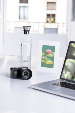 Digital camera, laptop, water carafe and framed picture of water lilies in pond