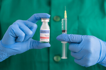 Woman in protective wear holding covid-19 vaccine and syringe