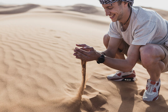 Happy male tourist playing with sand at desert in Dubai, United Arab Emirates