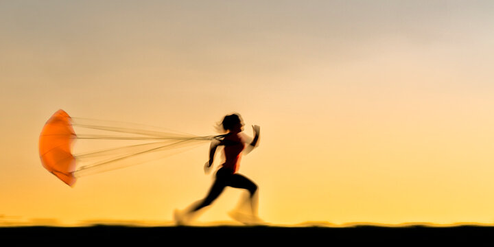 Silhouette young woman running with parachute during sunset