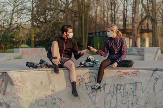 Woman giving man hand sanitizer while sitting at skateboard park during COVID-19
