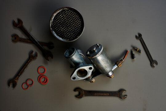 Top view of vintage carburetor with tools in front of grey background
