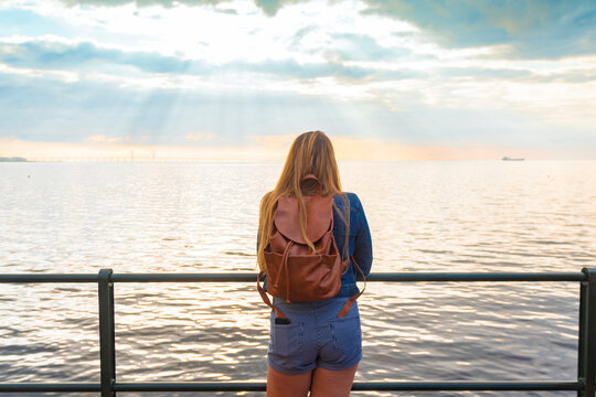 Rear view of woman with backpack standing at railing by sea against sky