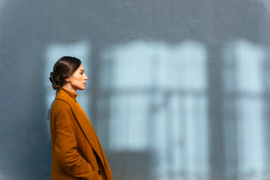 Woman wearing yellow winter coat while standing by gray wall with hands in pocket