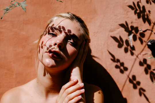 Sensual woman against wall with leaves shadow on face