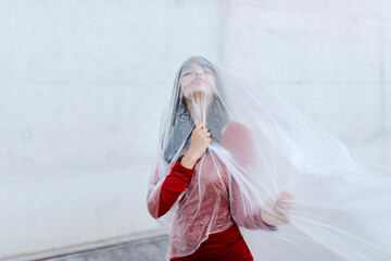 Woman wearing red dress while covering her body and face in plastic against concrete wall