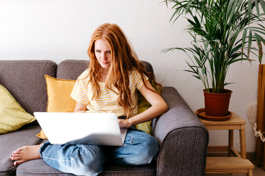Young woman using laptop while sitting on sofa at home