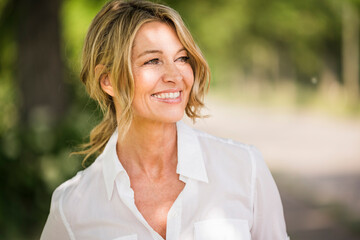 Thoughtful mature businesswoman smiling outdoors during sunny day