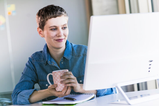 Smiling businesswoman at desk in office looking at computer screen