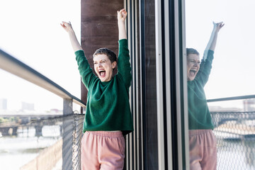 Cheerful businesswoman with arms raised screaming while standing in balcony