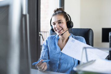 Businesswoman with paper discussing while looking at computer in office