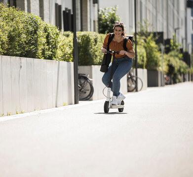 Smiling woman riding electric push scooter on road during sunny day