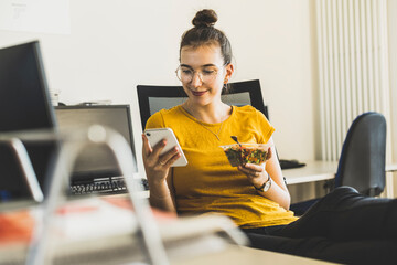 Smiling businesswoman using mobile phone during lunch break at office