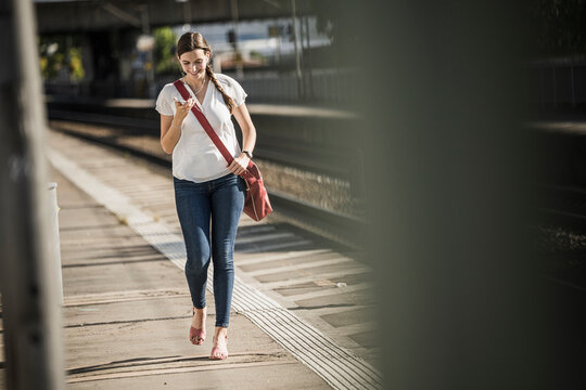Young woman listening music through mobile phone while walking on railroad station platform