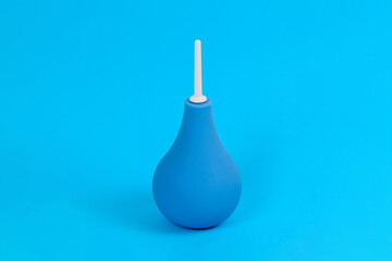 Blue pear-shaped enema with white tip on light blue background. Colon cleansing concept. Background for medical announcement