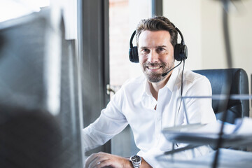 Smiling businessman wearing headphones sitting at office