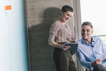 Smiling female entrepreneur discussing over digital tablet with businessman in office