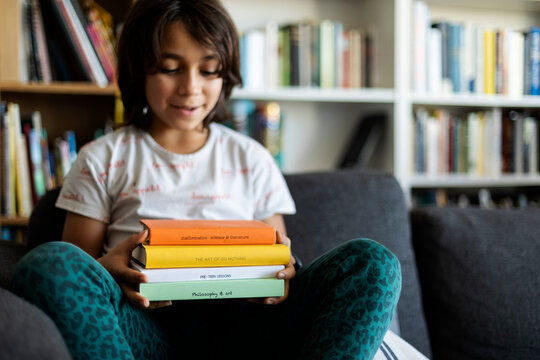 Boy sitting on couch at home holding stack of four books