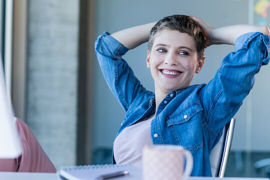 Smiling relaxed businesswoman sitting at desk in office