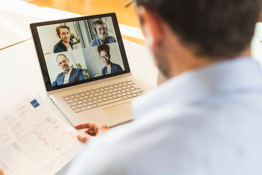 Businessman holding paper while attending video conference with team on laptop at office