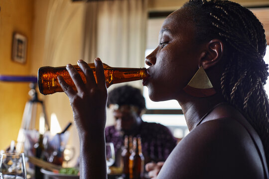 Close-up side view of young woman drinking beer from bottle while enjoying lunch at home