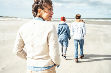 Portrait of young woman walking on sandy beach with two people in background